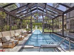 an indoor swimming pool surrounded by glass walls and doors with chairs around it, in front of a house