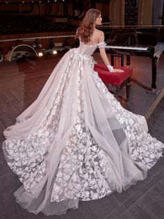 a woman in a wedding dress is sitting on a red chair and looking at the piano