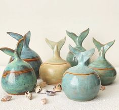 five ceramic vases sitting next to each other on a white surface with shells scattered around them