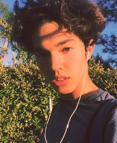 a young man wearing headphones and looking at the camera with trees in the background