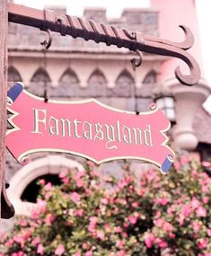 a pink sign hanging from the side of a wooden pole with flowers in front of it