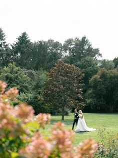 a bride and groom standing in the middle of a lush green field surrounded by trees