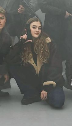 a woman sitting on the ground while holding a cell phone to her ear with soldiers behind her