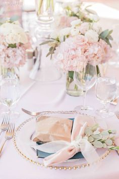 the table is set with pink and white flowers in vases, silverware, and napkins