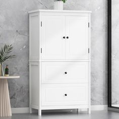 a white cabinet with two drawers next to a mirror and vase on the floor in front of it