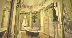 an ornate bathroom with tub, chandelier and green curtains on the window sill