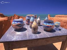 there are many vases sitting on the table by the water's edge and one is empty