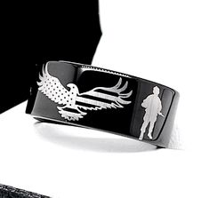 a black and white photo of a cuff bracelet with an eagle on the front, two men's silhouettes in the background