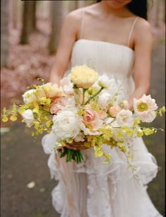 a woman holding a bouquet of flowers in her hand and wearing a white dress with ruffles