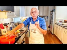 an old man in the kitchen with his apron on and pointing at something he is holding