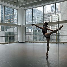 a ballerina is practicing her moves in an empty room with large windows and high rise buildings