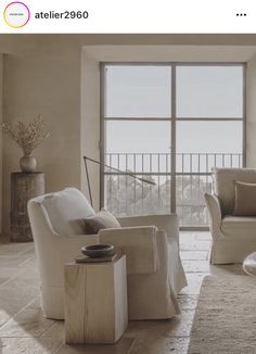 a living room filled with white furniture next to a large window and a rug on the floor