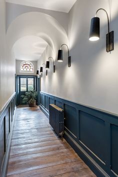 the hallway is lined with blue paneling and wooden flooring, along with three black wall sconces