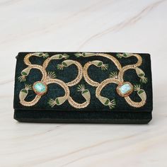 This book bag is a unique and beautiful piece of accessory, made from luxurious green velvet that gives it a rich and soft texture. The turquoise stone inlaid in the center of the bag adds a pop of color and elegance, making it stand out from the rest. The floral pattern embellished with metal threads is intricate and sophisticated, and it has been delicately handcrafted to add a touch of glamour to the bag. The metal threads, shining under the light, bring an extra touch of luxury and add to the overall aesthetic of the bag. The bag is spacious enough to carry all your essentials, such as books, notebooks, and a small laptop. Its generous size makes it ideal for use as a school bag, a work bag, or for traveling. The green velvet and turquoise stone combination makes this book bag not only Embroidered Shoulder Bag, Zardozi Work, Handmade Clutch, Small Laptop, Clutches For Women, Handcrafted Bags, Stone Work, Work Bag, Book Bag