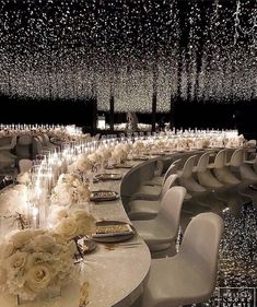 a long table with white chairs and flowers on it is surrounded by chandeliers