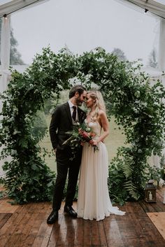 a bride and groom standing in front of an arch with greenery at their wedding