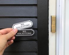 a hand holding a no soliciting sticker next to a door with the words no soliciting and no soliciting on it