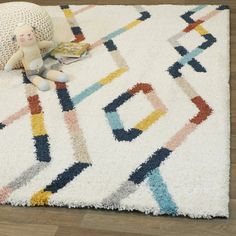 a child's stuffed animal sitting on top of a white rug next to a pillow