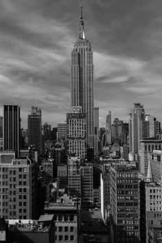 a black and white photo of the empire building in new york city, with dark clouds overhead