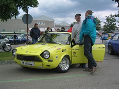 two men standing next to a yellow car