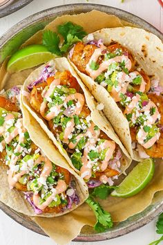 three fish tacos on a plate with limes and cilantro