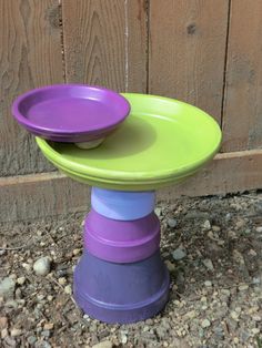 purple and green plates stacked on top of each other in front of a wooden fence