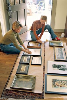 two women are sitting on the floor looking at pictures and framed photographs in front of them