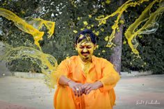 a man with yellow paint on his face and hands, standing in front of trees