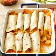 several burritos in a casserole dish on a table next to sliced cucumbers