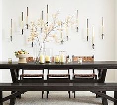 a wooden table with candles and vases on it in front of a white wall