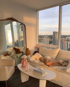 a woman laying on a couch in front of a large window next to a dog