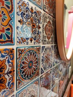 colorful tiles are arranged on the wall in this bathroom, with a mirror above them