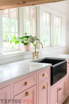 a pink kitchen with gold faucet and white countertops in front of windows