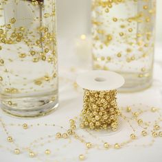 two vases filled with gold beads and spools of thread on a table