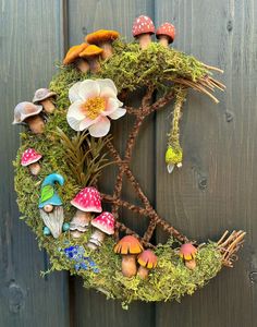 a wreath made out of moss with mushrooms and flowers on it, hanging from a wooden fence