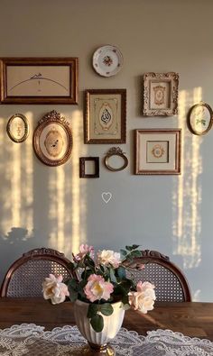 there is a vase with flowers on the table in front of many framed pictures and clocks