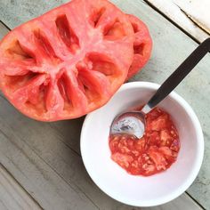 a tomato is cut in half with a knife and sauce in a white bowl on a wooden table