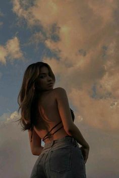 a woman standing in front of a cloudy sky with her back turned to the camera