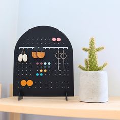 a potted cactus sitting on top of a wooden table next to a wall mounted earring holder