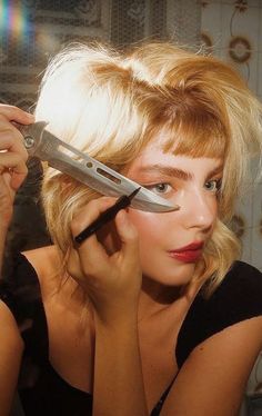 a woman holding a knife in front of her face and looking at herself through the mirror