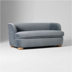 a grey couch sitting on top of a white floor next to a gray wall and wooden legs