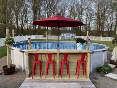 an above ground swimming pool with red chairs and umbrella over the bar, surrounded by trees