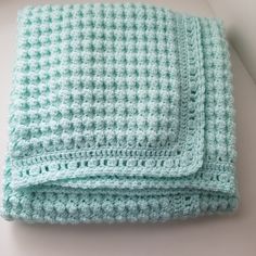 a green crocheted blanket sitting on top of a white table next to a window