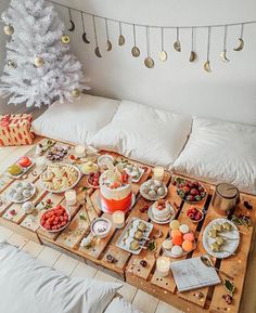 a table with food on it next to a white christmas tree in the corner,