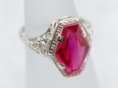 This fantastic Art Deco era ring is iconic of the early 1900s, with a perfectly preserved synthetic ruby gemstone set at its center. In the Victorian era, transportation was far more expensive than it is now. Rubies had to be brought from Burma, and Emeralds from South America. This cost translated into the price of the stones, making them far too expensive for the average consumer. In response, jewelers found interesting ways to make natural stones go a little farther. Synthetics were created: stones faceted from crystals grown in laboratories. These remained popular right through the Art Deco era. Metal: 18K White GoldGem: Synthetic Ruby Gem Measurements: 12.0 x 8.1 mm, Fancy CutRing Size: 4Marks: “18” Stamped on the inside band Victorian Wedding Signet Ring With Gemstone, Antique Gemstone Signet Ring For Wedding, Vintage Rings With Octagon Center Stone, Vintage Octagon Ring With Center Stone, Fine Jewelry Ruby Signet Ring For Formal Occasions, Victorian Gemstone Signet Ring For Formal Events, Victorian Gemstone Signet Ring For Formal Occasions, Ruby Signet Ring Fine Jewelry For Formal Events, Classic Ruby Ring With Diamond Cut