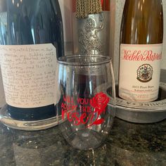 two wine glasses with writing on them sitting on a counter top next to bottles of wine