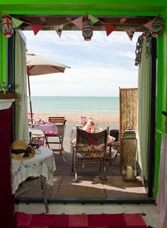 an open door leading to the beach with people sitting at tables and chairs under umbrellas