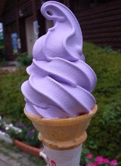 a purple ice cream cone sitting on top of a wooden pole in front of flowers