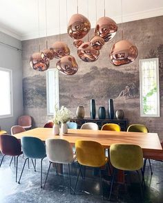 a dining room table surrounded by chairs and hanging lights above it is an art work on the wall