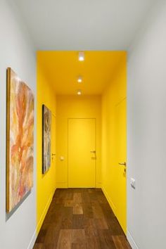 an empty hallway with yellow walls and wood flooring on the other side as well as two paintings hanging on the wall